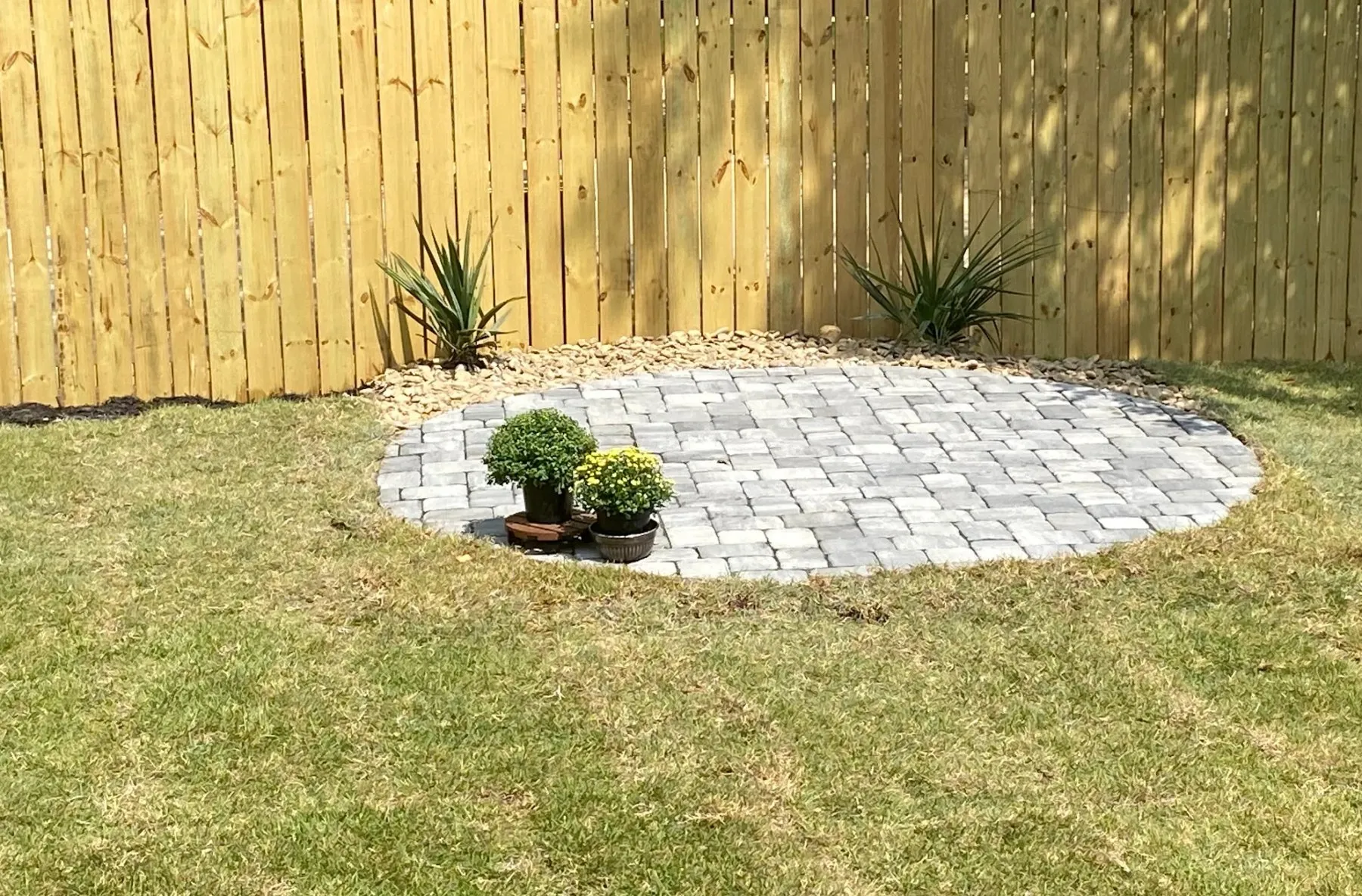 Circular paver patio with mulch and plantings against a privacy fence