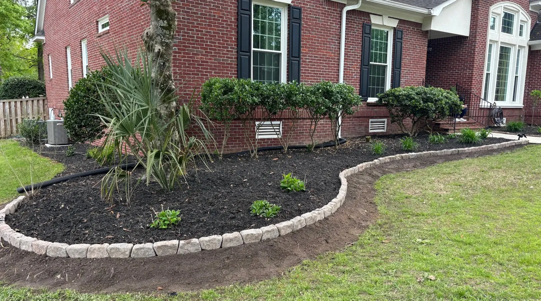 Brick home with a new stone-bordered bed, black mulch and fresh plantings