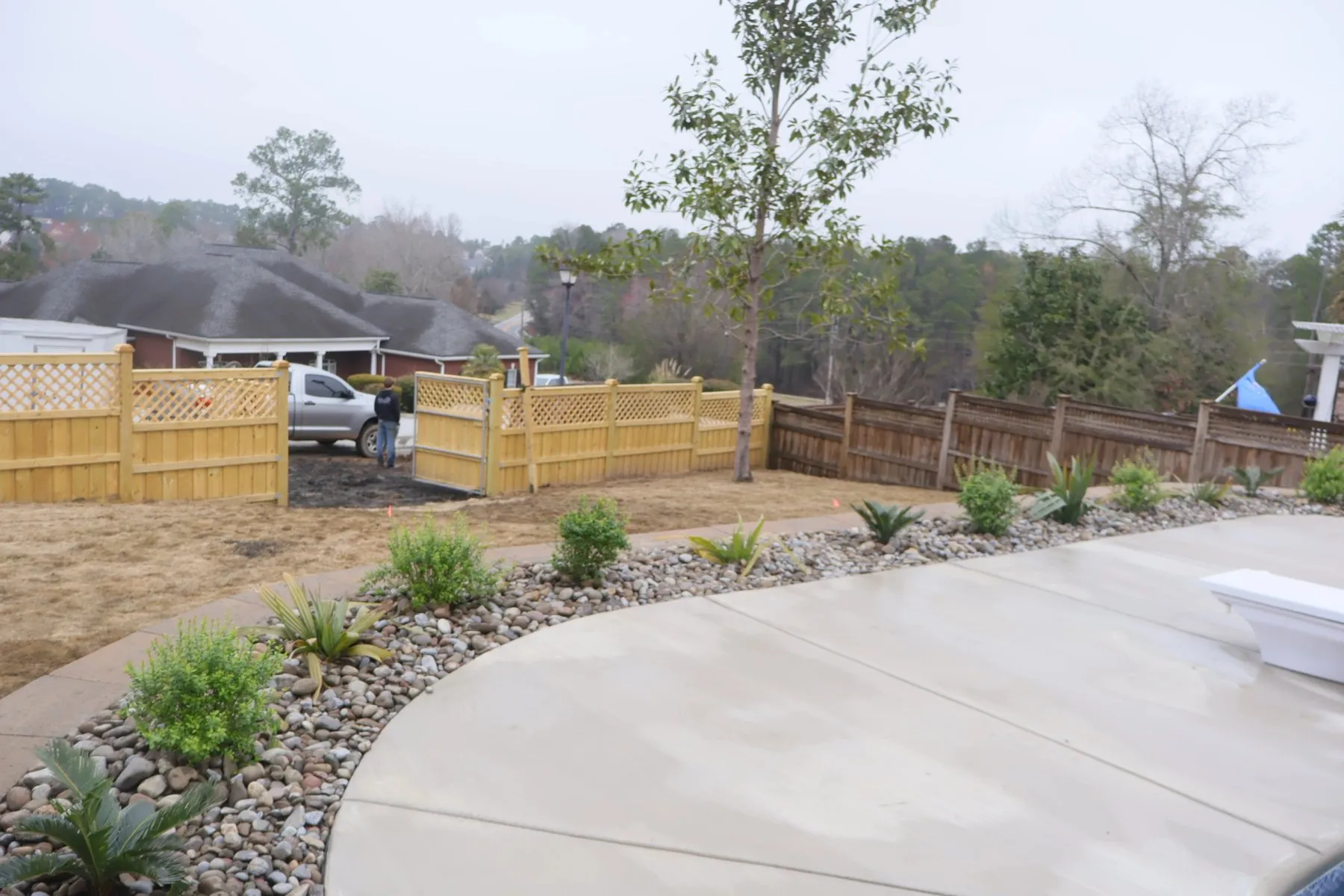 Curved concrete walkway with new plantings along a wooden privacy fence