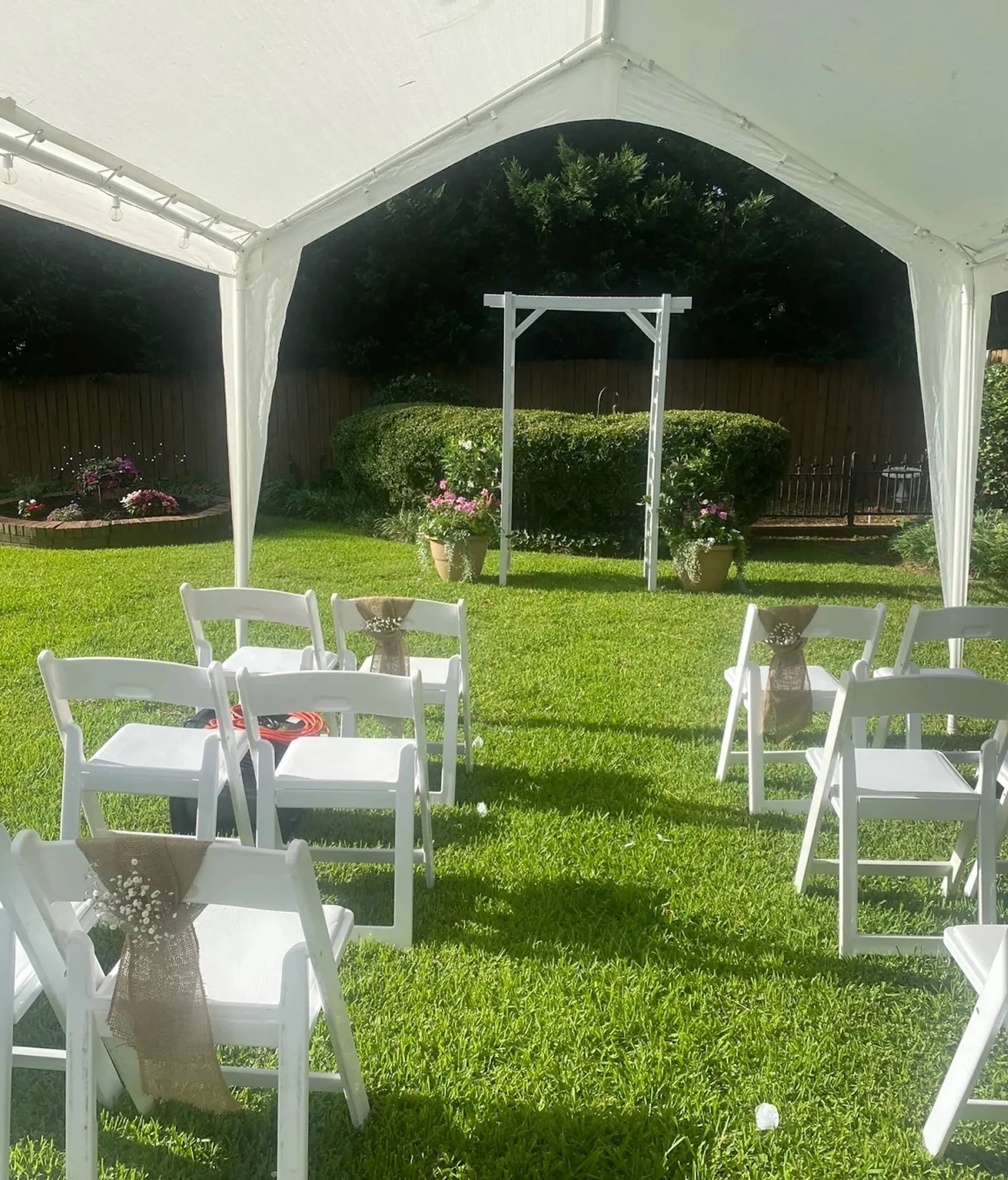 Manicured backyard lawn set up with white chairs and an arbor for a wedding